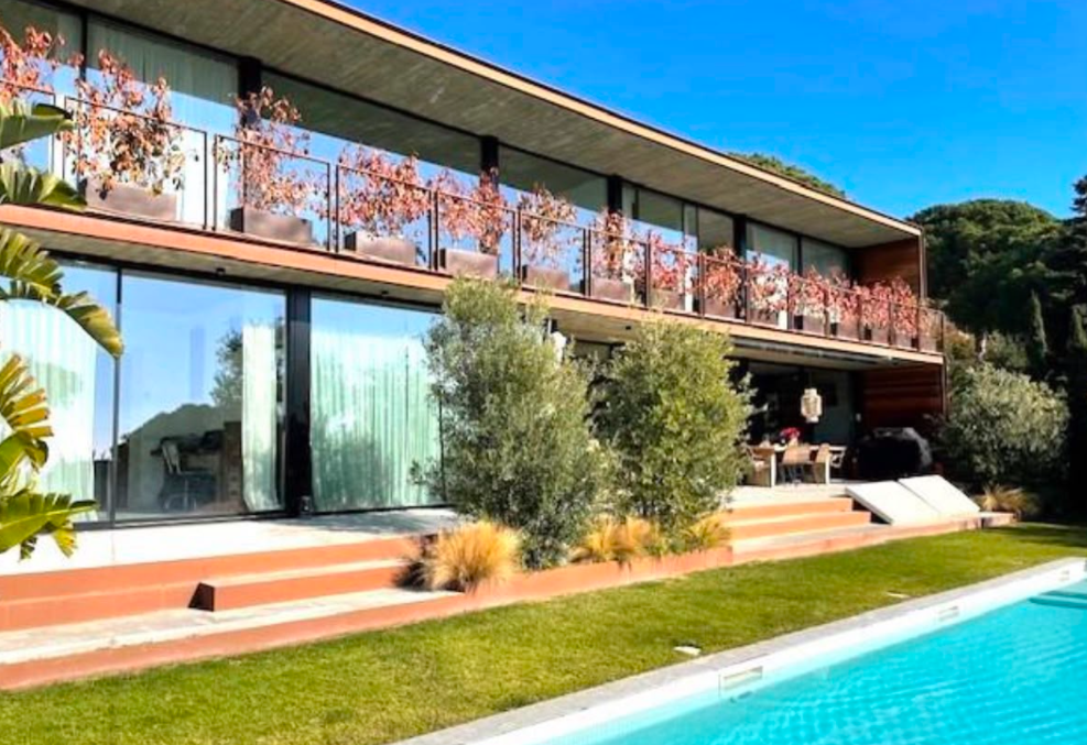 Vista exterior de la vivienda con piscina, jardín y fachada de cristal
