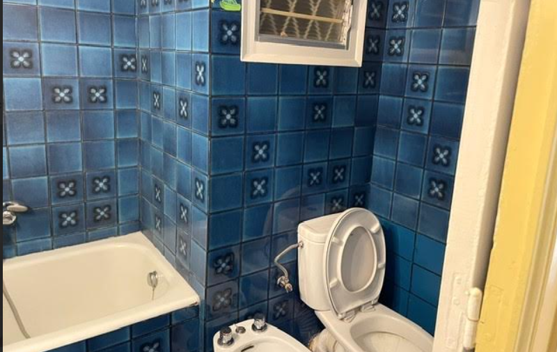 Baño antiguo con alicatado azul, bañera y sanitarios originales antes de la reforma