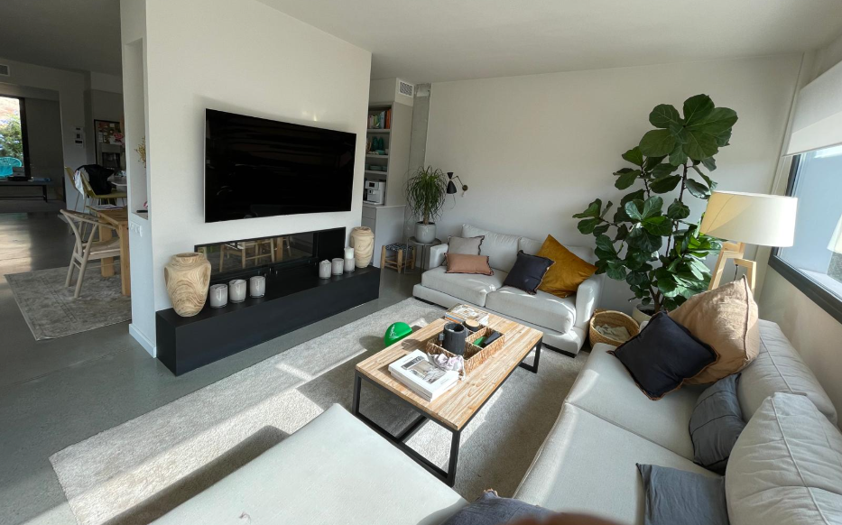 Salón reformado con chimenea, sofás claros, mesa de centro de madera y planta decorativa
