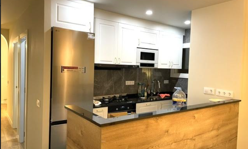 Cocina reformada con barra de madera, encimera oscura y muebles blancos