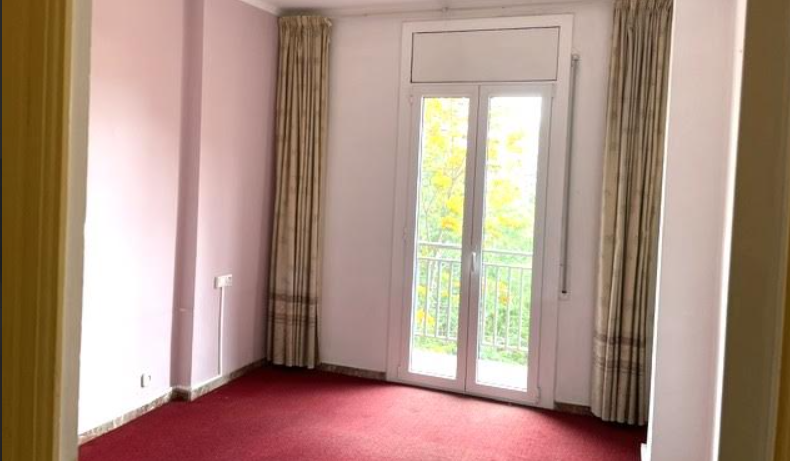 Habitación antes de la reforma con moqueta roja, cortinas antiguas y salida al balcón
