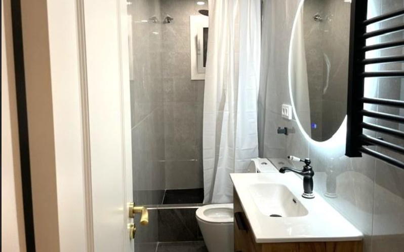 Baño reformado con ducha de obra, gres gris, espejo circular retroiluminado y mueble de madera