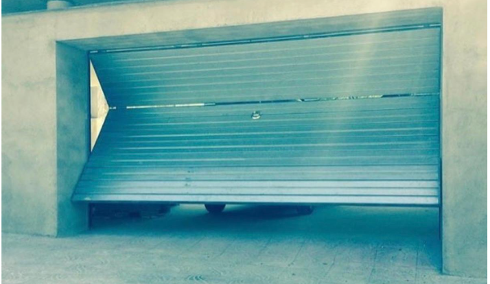 Puerta basculante metálica de acceso al parking en fachada de hormigón